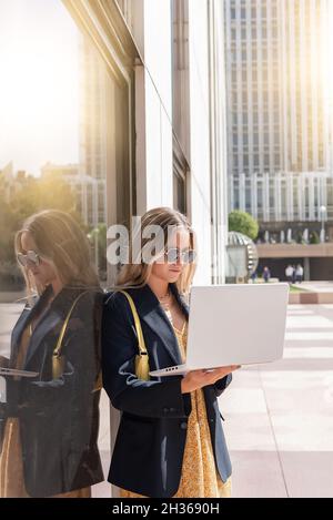 Giovane bella donna d'affari che indossa occhiali da sole utilizzando il suo laptop fuori dall'ufficio Foto Stock