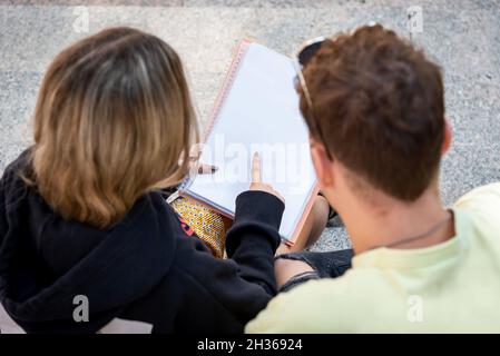 Due giovani studenti universitari, un uomo e una donna, si siedono su una scala rivedendo le note di classe. La donna punta a qualcosa in particolare nel libro Foto Stock