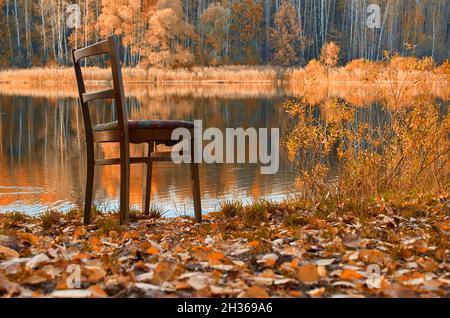 Una vecchia sedia di legno si erge sulla riva del lago Foto Stock