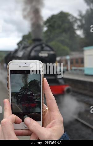 Treno a vapore NYMR su dispositivo mobile e in background - Grosmont Station - Heritage Railway - Modern Day Technology - iPhone 7 - nuovo & vecchio - Regno Unito Foto Stock