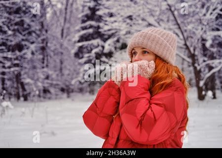 Una donna sorridente si avvolge in abiti che si riscaldano in una foresta invernale con alberi nella neve Foto Stock