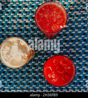 Vista dall'alto di tre diversi deliziosi cocktail estivi con le lecubes sul tavolo, bicchieri con bevande rinfrescanti alla frutta su tovaglia blu Foto Stock