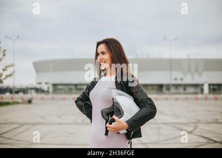 Vista dal basso di giovane donna attraente biker indossando casco di sicurezza per bicicletta mentre si trova in piedi allo stadio vuoto all'aperto, bella motociclista femminile a dres Foto Stock