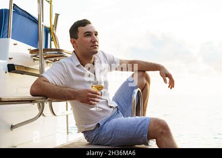 Giovane uomo che tiene un bicchiere di vino su un ponte aperto di una nave da crociera Foto Stock