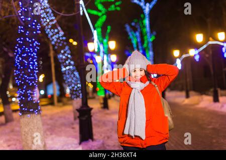 Felice divertente giovane donna con abiti invernali sfondo sera luci città illuminazione. Natale e inverno concetto. Foto Stock