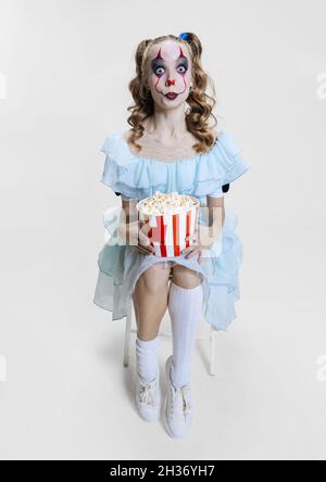 Immagine concettuale della giovane ragazza che indossa un abito di Halloween di pagliaccio da ballo con un make-up spettrale isolato su sfondo grigio. Foto Stock