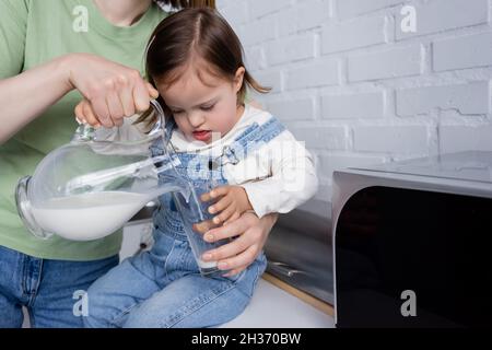 Donna che versa il latte in vetro vicino alla figlia con sindrome di Down in cucina Foto Stock