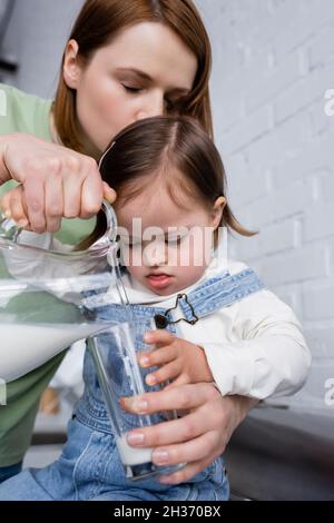 Donna che versa il latte vicino al bambino con sindrome di Down in cucina Foto Stock