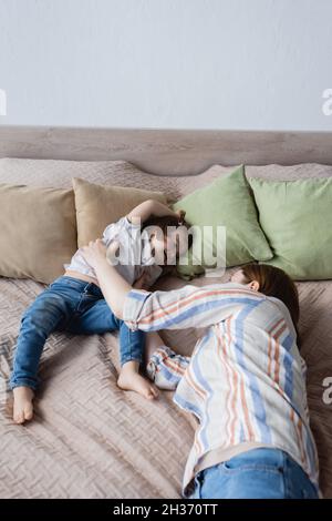 Donna sdraiata vicino alla figlia del bambino con sindrome di Down sul letto a casa Foto Stock