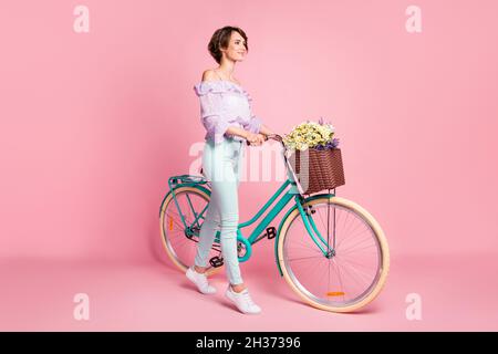 Ritratto fotografico a tutta lunghezza di donna con bicicletta a piedi isolato su sfondo rosa pastello Foto Stock