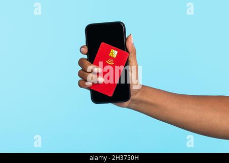 Irriconoscibile donna nera millennial con carta di credito e cellulare su sfondo blu, mockup per il design Foto Stock