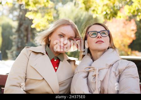 Due belle amiche mature che si godono una calda giornata d'autunno nel parco insieme Foto Stock