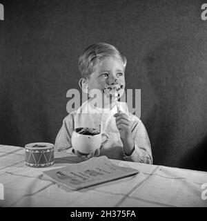 Ein kleiner Junge isst eine Tasse Schokoladenpudding und schmiert sich damit richtig ein, Deutschland 1940er Jahre. Un ragazzino che mangia un budino di cioccolato ed è completamente spalmato, Germania 1940. Foto Stock