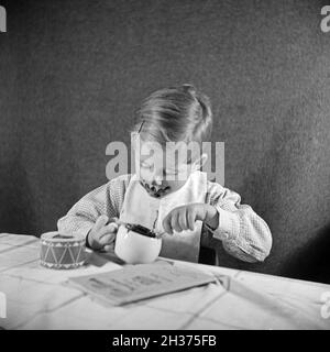 Ein kleiner Junge isst eine Tasse Schokoladenpudding und schmiert sich damit richtig ein, Deutschland 1940er Jahre. Un ragazzino che mangia un budino di cioccolato ed è completamente spalmato, Germania 1940. Foto Stock