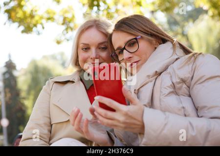 Inquadratura ad angolo basso di due donne mature che utilizzano lo smartphone nel parco Foto Stock
