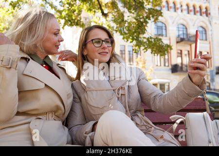 Donna di mezza età che usa lo smartphone per prendere selfie con il suo amico nel parco Foto Stock