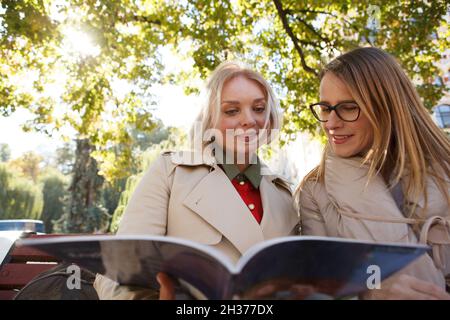 Inquadratura a basso angolo di due amici femminili che leggono insieme un libro, preparandosi per gli esami all'aperto Foto Stock