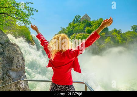 Donna che scherza la cascata svizzera Rheinfall in Svizzera. La cascata più potente e grande d'Europa, situata nei cantoni di Sciaffusa Foto Stock