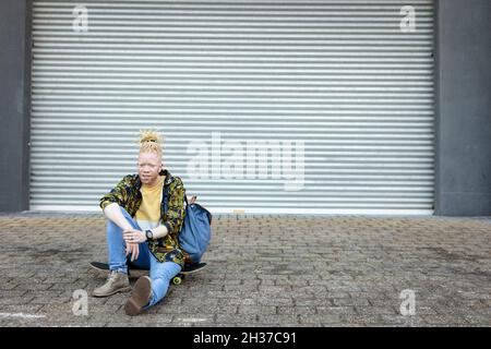 Ritratto di un uomo afro-americano con readlock seduto skateboard Foto Stock