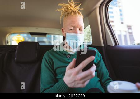 Albino african american uomo indossare maschera viso seduta in auto utilizzando smartphone Foto Stock