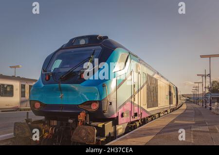 Locomotiva moderna con insoliti stand su una piattaforma ferroviaria. Un basso sole serale brilla sul suo lato e le ombre cadono sulla piattaforma. Foto Stock