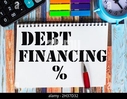 Testo debito finanziario su foglio e tavolo di legno sveglia, calcolatrice, adesivi Foto Stock