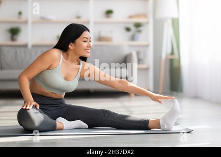 Sport giovane bella donna asiatica formazione a casa, stretching in soggiorno Foto Stock