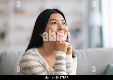 Ritratto di sognante giovane bella Asiatica Lady rilassante in interni domestici Foto Stock