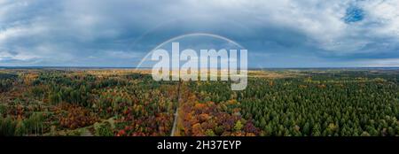 Panoramica arcobaleno doppio di una foresta colorata in autunno con la vista sullo skyline bavarese di Monaco sullo sfondo. Foto Stock