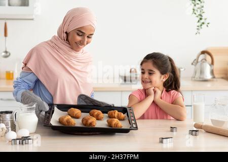 Pasta fatta in casa. Madre musulmana in cottura hijab con figlia piccola in cucina Foto Stock