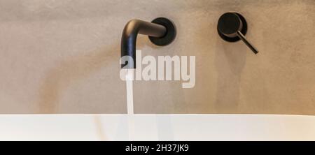 Rubinetto con lavandino dal design moderno, dettagli interni del bagno. Rubinetto nero aperto montato a parete su lavandino bianco e acqua corrente, striscione, spazio copia Foto Stock