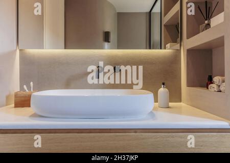 Lavandino in bagno su banco in marmo bianco, rubinetti neri su parete grigia, specchio e luce lineare a LED. Accessori e attrezzature moderne, interni minimi Foto Stock