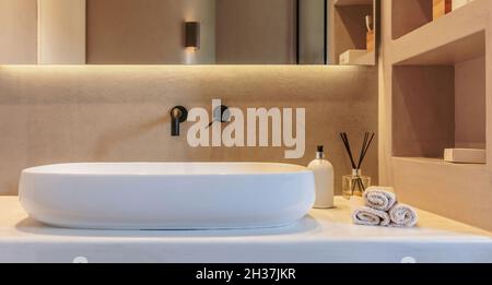 Interni bagno dal design minimalista. Lavabo rotondo su bancone in marmo bianco, rubinetti neri su parete grigia, specchio e luce lineare a LED. Accessori moderni A. Foto Stock