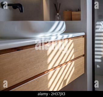 Lavandino in bagno su bancone in marmo bianco, rubinetti neri a parete, cassetto in legno e decorazioni. Interni dal design minimalista e moderno. Foto Stock