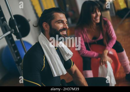 Bella coppia pulisce il sudore dopo una sessione di allenamento. Uomo e donna sportivi alla fine dell'allenamento in palestra. Atleti sudati con asciugamano in mano Foto Stock