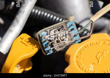 Piccolo componente elettronico polveroso su una sonda dell'olio e tappo dell'olio sotto il cofano aperto di un'auto. Primo piano in una giornata di sole Foto Stock