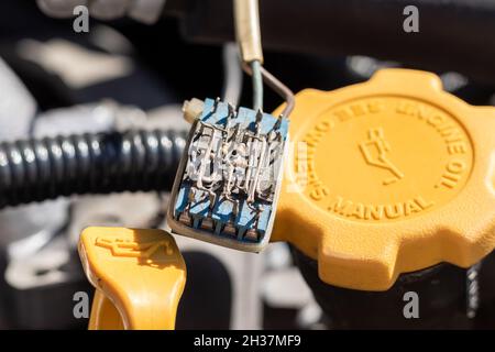 Piccolo componente elettronico polveroso su una sonda dell'olio e tappo dell'olio sotto il cofano aperto di un'auto. Primo piano in una giornata di sole Foto Stock