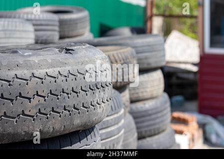 Vecchi pneumatici usati per auto impilati l'uno sull'altro vicino al negozio di pneumatici. Messa a fuoco selettiva. Primo piano. Sfondo sfocato Foto Stock