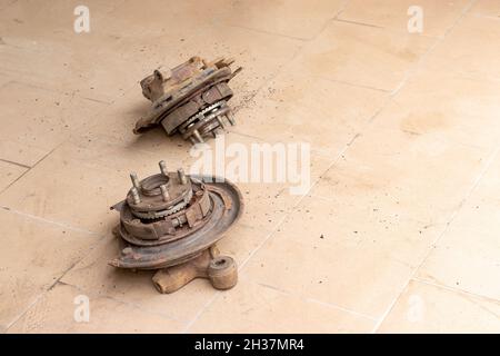 Due vecchi mozzi posteriori, usati, arrugginiti, sui quali sono visibili le pastiglie del freno di stazionamento, senza disco del freno sul pavimento mattonellato beige del repai auto Foto Stock