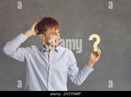 Uomo serio e premuroso che guarda la figura di domanda di legno in mano studio scatto Foto Stock