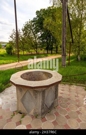 Calcestruzzo bene telaio, punto di presa d'acqua dal bordo della strada. Giardino sullo sfondo. Lozova, Gagazuzia, Repubblica di Moldavia. Foto Stock