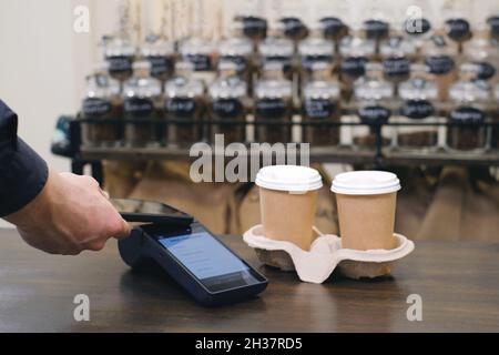 Cliente che utilizza lo smartphone e la tecnologia nfs per pagare il barista per l'acquisto con il telefono in un bar per il caffè. Transazione sicura Foto Stock