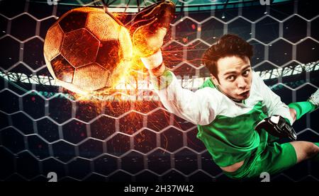 Primo piano di una scena calcistica durante la partita notturna con un portiere che cerca di catturare una palla ardente Foto Stock