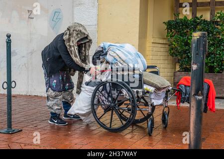 Giù e fuori donna che spinge una sedia a rotelle con i suoi effetti personali sul marciapiede su state Street. Foto Stock