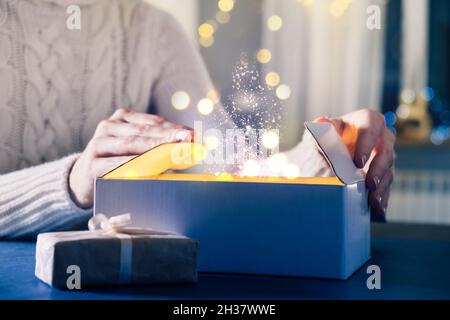 La persona apre il dono, miracoli e desideri si avverano alla vigilia di Natale. Primo piano delle mani e regalo di Capodanno a casa di notte. Sfondo magico con polvere Foto Stock