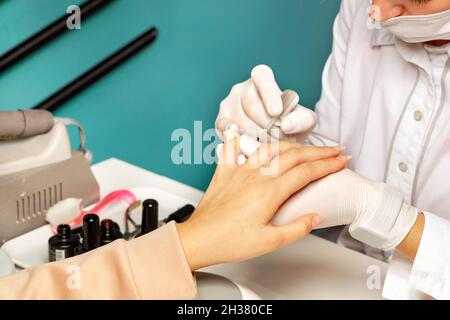 Un maestro estetista in una maschera protettiva conduce una sessione manicure per una giovane donna. Foto Stock