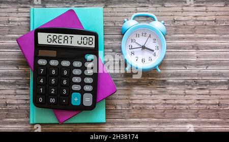 Ottimo lavoro scritto sul display della calcolatrice, che giace su cuscinetti colorati e uno sfondo di legno. Foto Stock