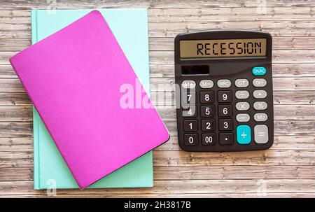 Recessione, il testo è scritto su una calcolatrice, ci sono notepad colorati accanto ad esso su un tavolo di legno. Foto Stock