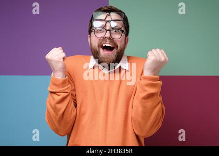 Strano uomo messo su tre paia di occhiali, è piacevolmente sorpreso, si rallegra, ride e fa un gesto di vittoria con le mani. Foto Stock