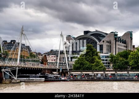 Una Uber Boat passa sotto i ponti Hungerford/Golden Jubilee con la Charing Cross Station nel Backround, Londra, Regno Unito. Foto Stock